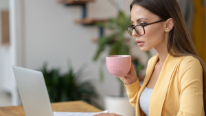Frau mit Kaffee in der Hand sitzt am Laptop zum digitalen Neujahrsbrunch
